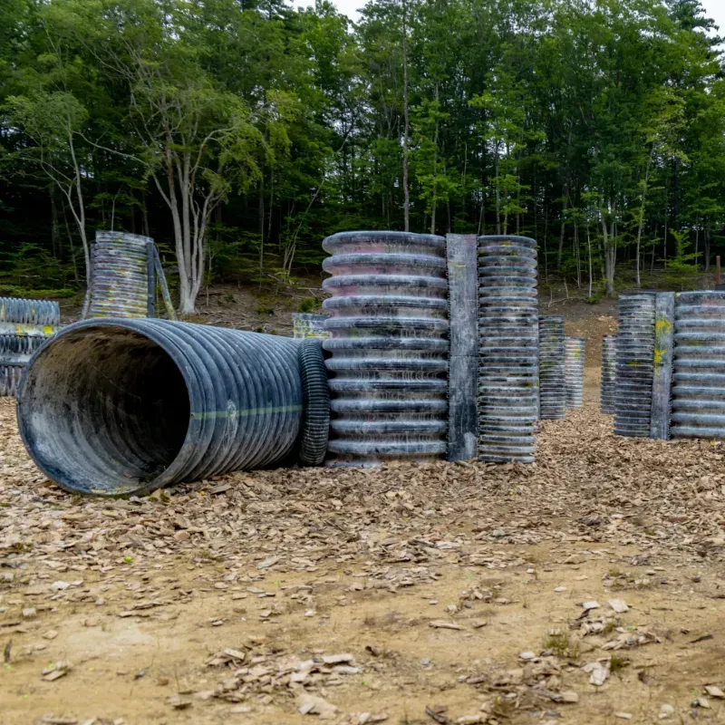 Paintball course with corrugated tubes and concrete barriers in a wooded area.