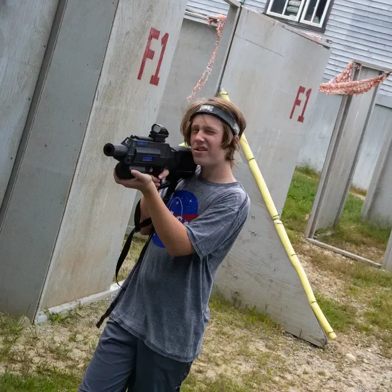Teenager holding a laser tag gun, aiming near wooden structures marked 