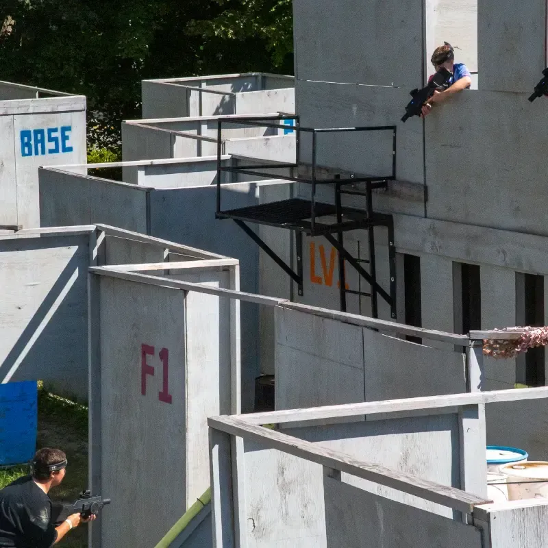 People playing a combat game at an outdoor arena with concrete structures, aiming toy guns.
