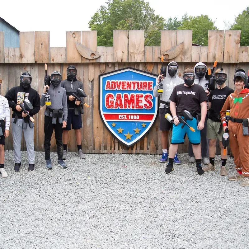 Group of paintball players in gear, posing in front of a sign at Adventure Games.