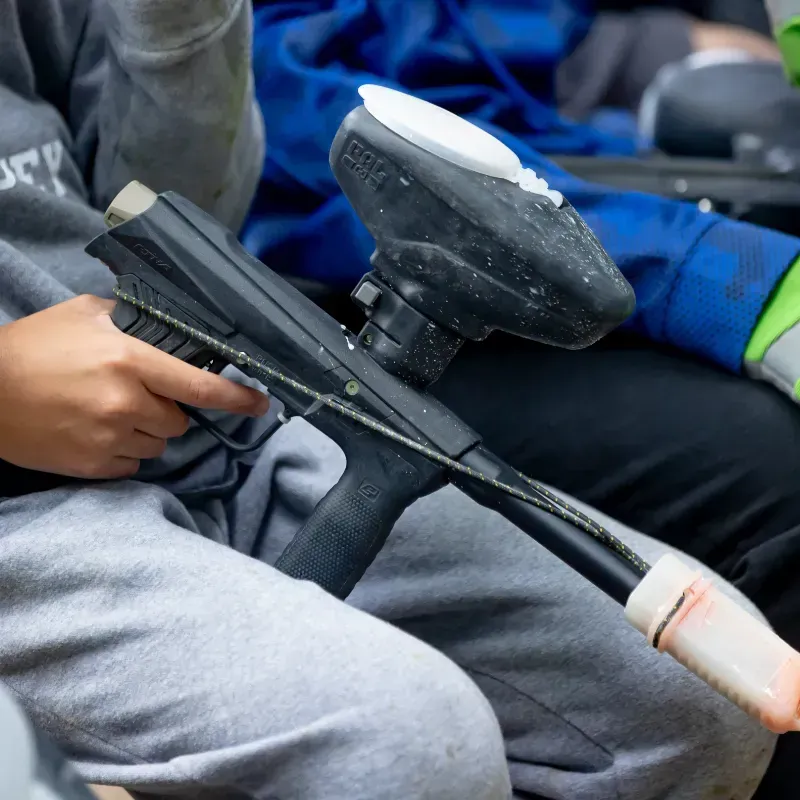 Person holding a black paintball gun; they are in gray sweatpants.