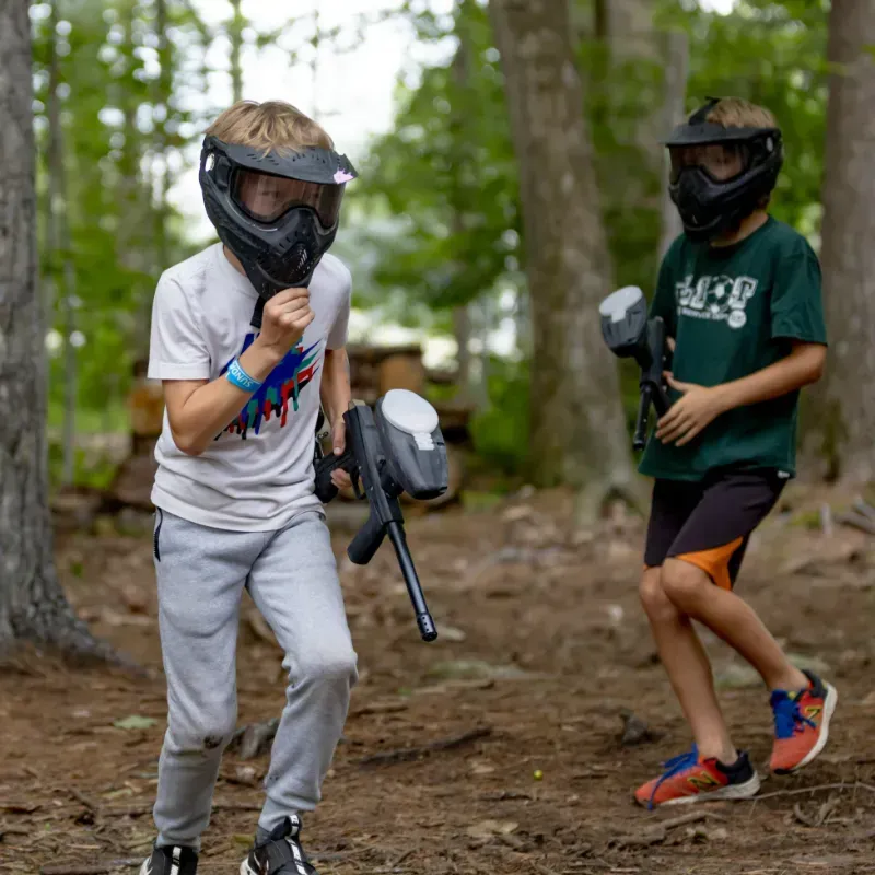 Two boys in paintball gear play in a forest.