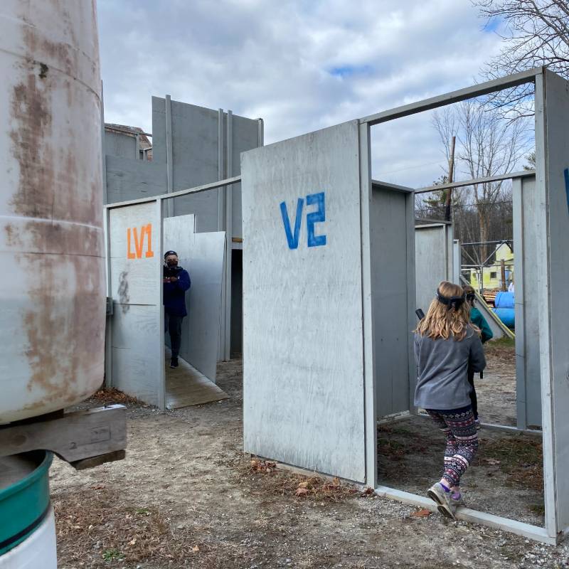 People playing laser tag in an outdoor arena with gray walls, labeled 