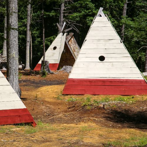 Three white pyramid-shaped structures with red bottoms stand in a wooded area.