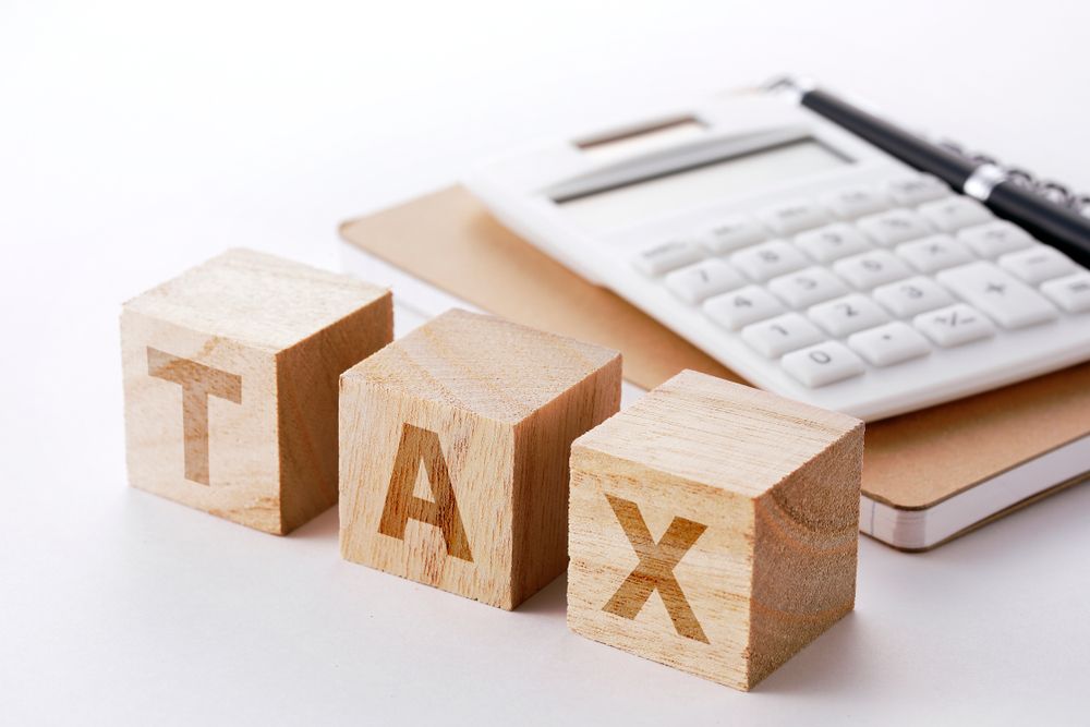 The word tax is written on wooden blocks next to a calculator and pen.