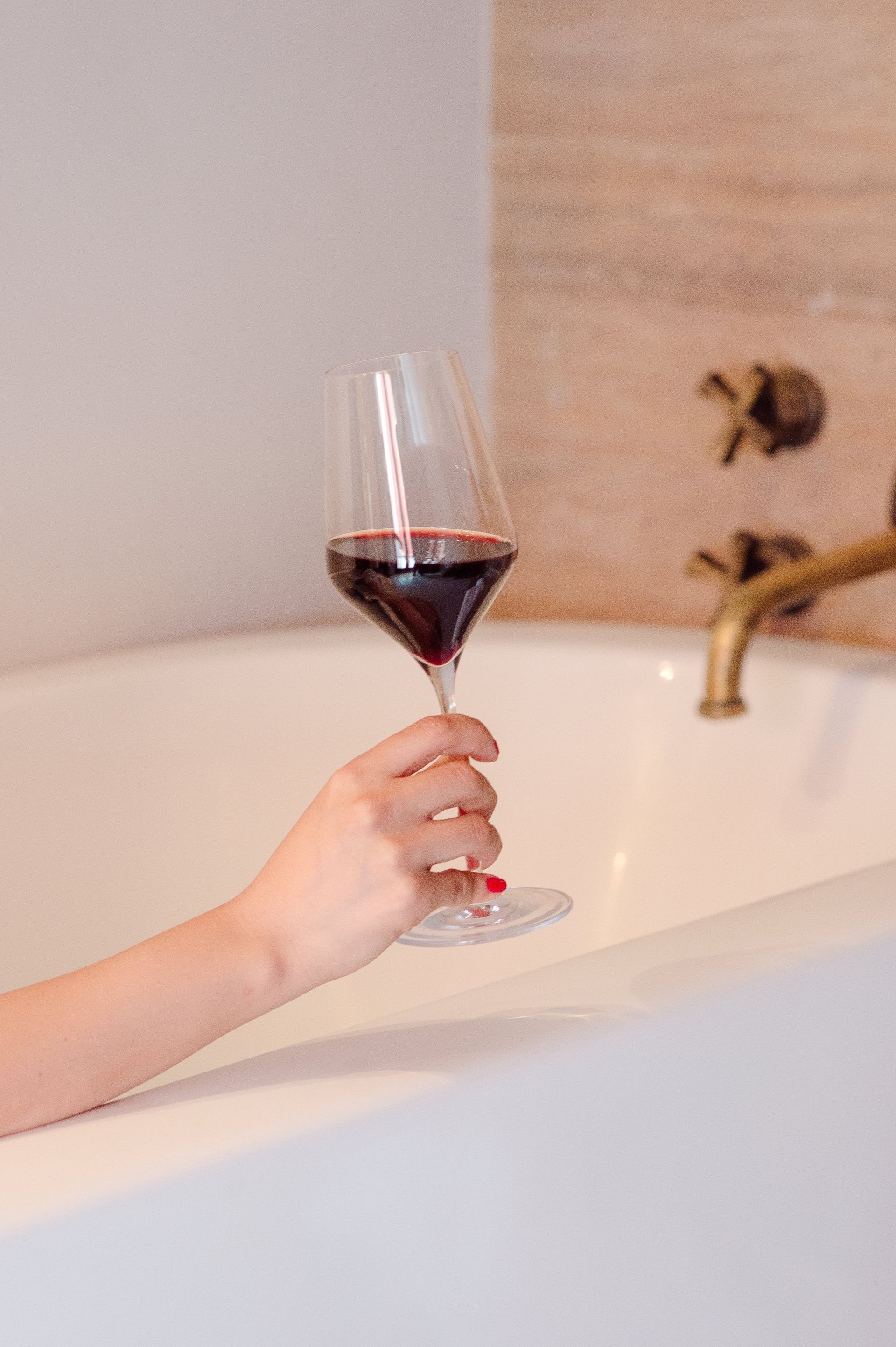 Una mujer se está bañando y sostiene una copa de vino tinto.