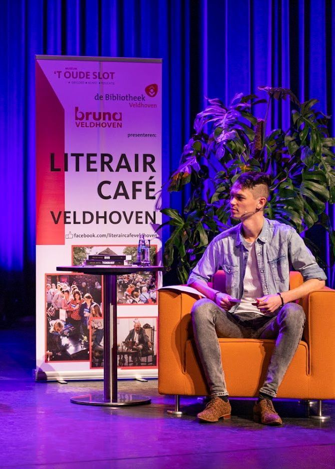 Mark van der Linden op een stoel met naast hem een banner over he Literair Café