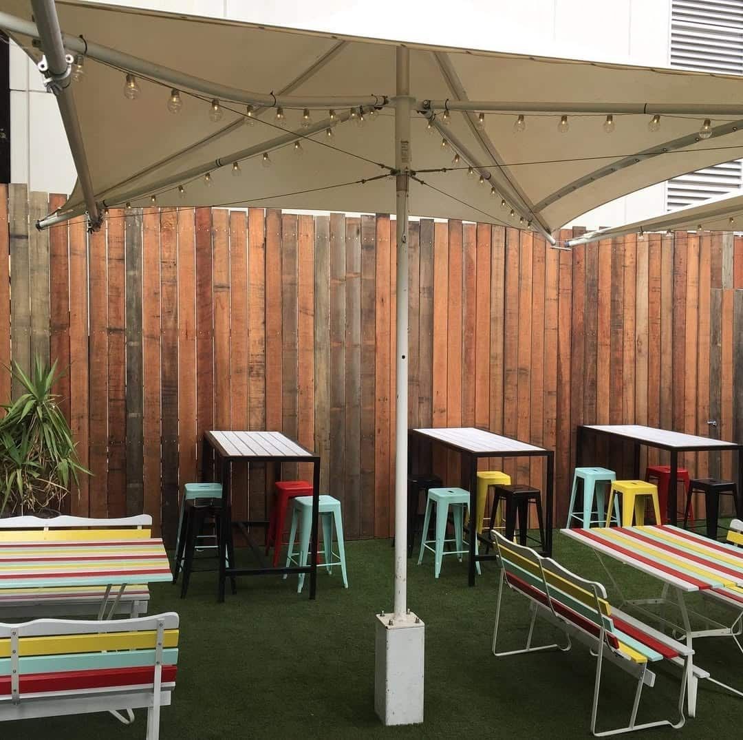 A large wooden fence with three tall tables and colourful stools — Flintoff Constructions in Charlemont, VIC