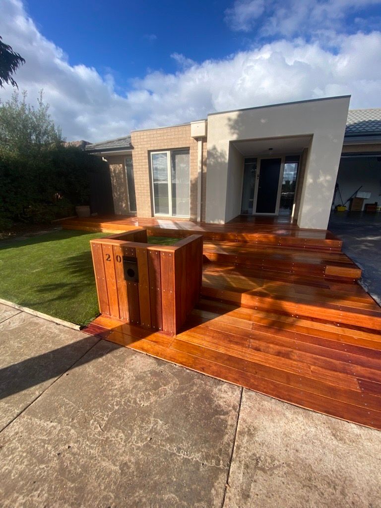 A wooden deck is being built under a pergola in a backyard.