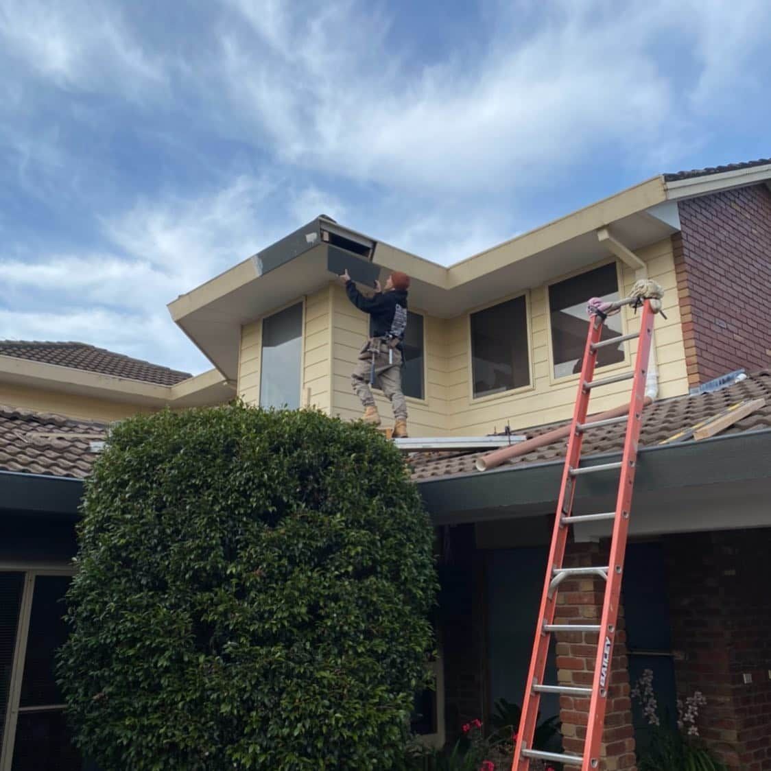 A Man on A Ladder Is Working on The Roof of A House — Flintoff Constructions in Charlemont, VIC