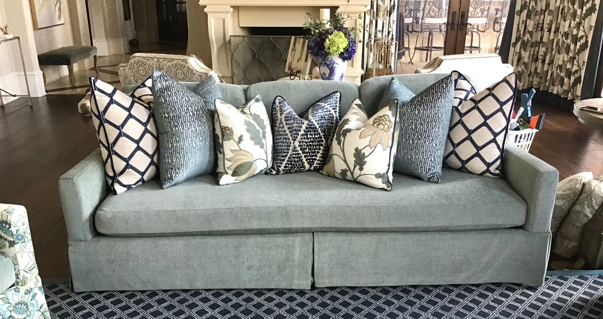 A light blue upholstered sofa with a skirt, arranged with a variety of patterned and solid decorative throw pillows.