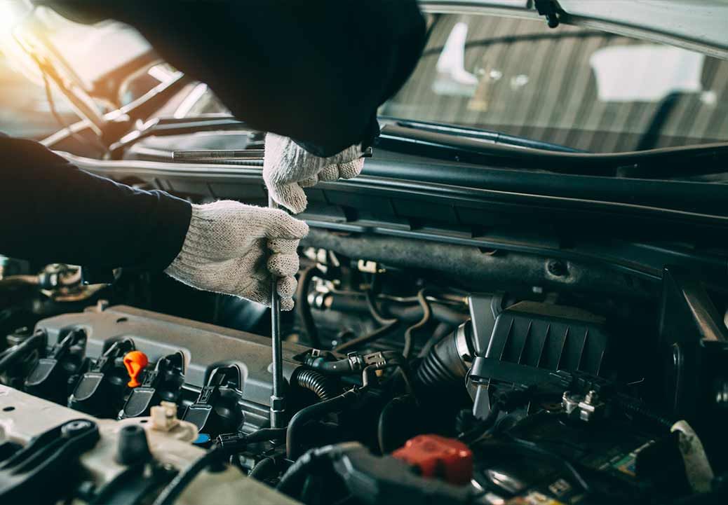 Mechanic working on a car engine with a wrench. Wearing gloves, indoors.