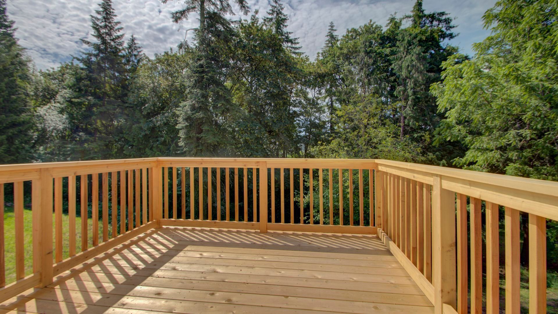 A wooden deck with a railing and trees in the background.