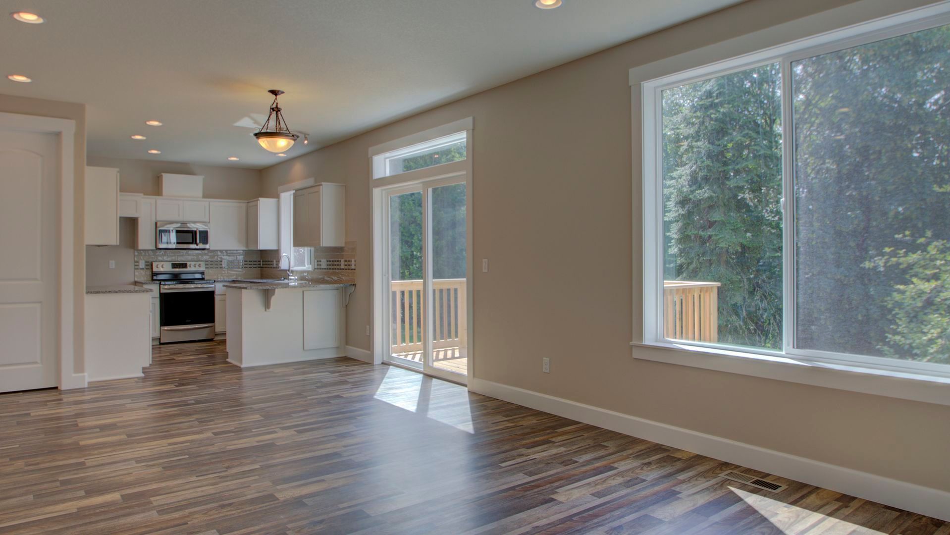 An empty living room with hardwood floors and sliding glass doors leading to a kitchen.