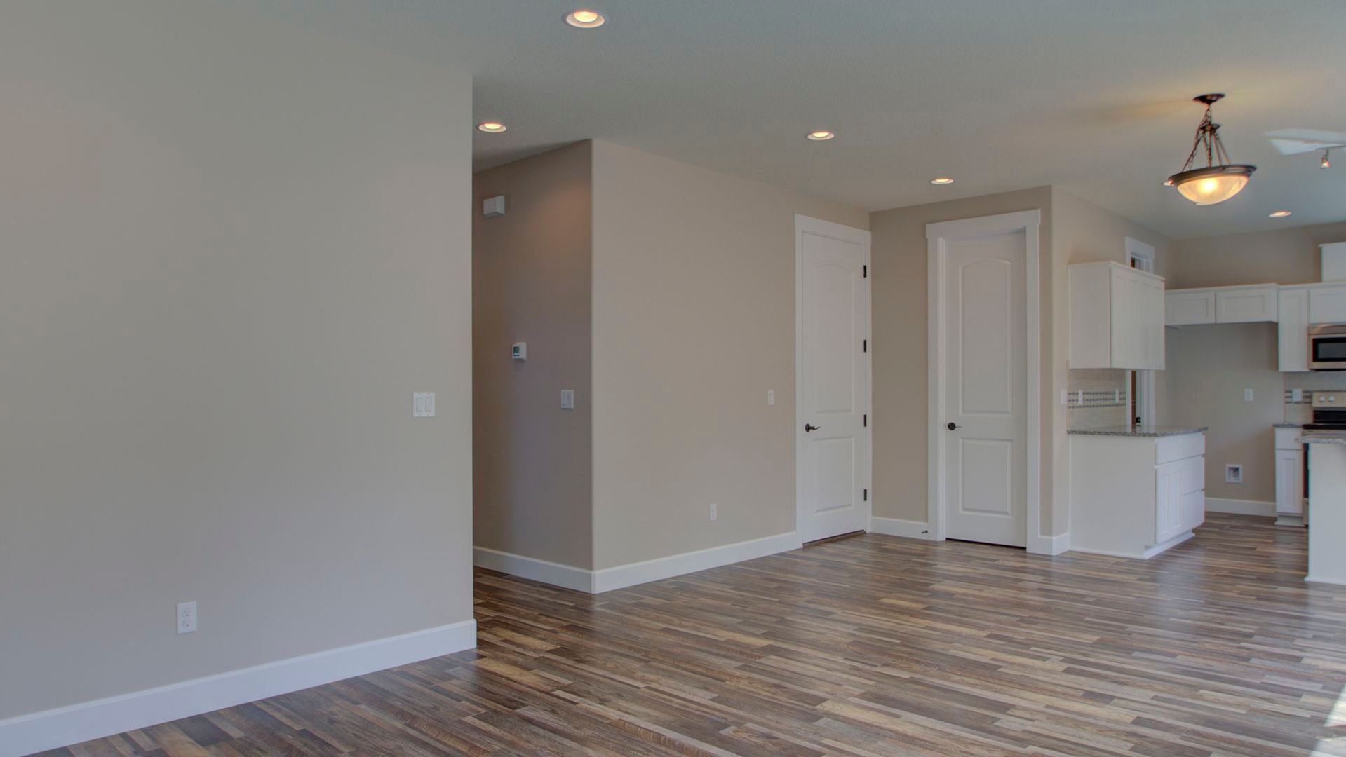 An empty living room with hardwood floors and a kitchen in the background.