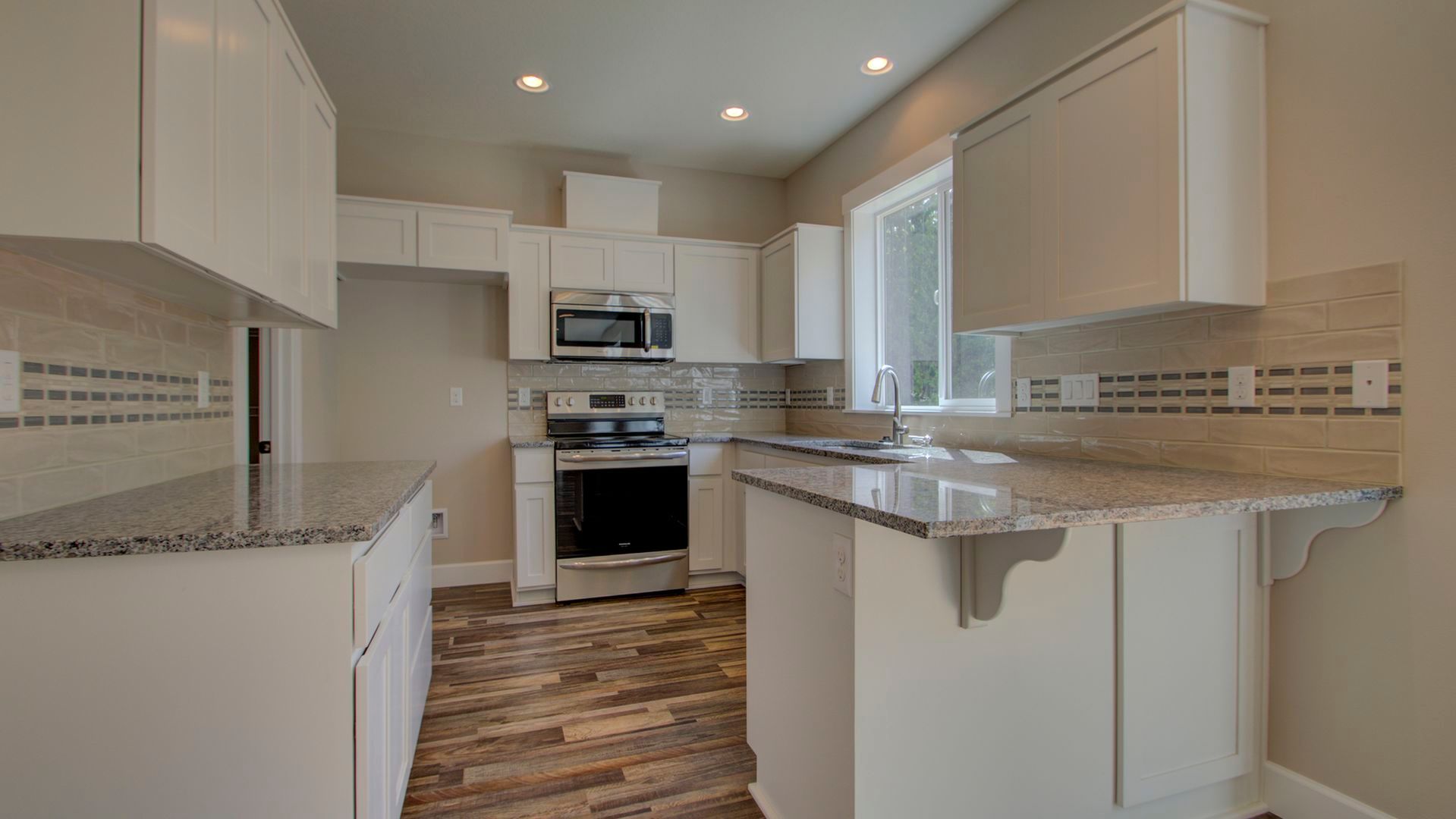 A kitchen with white cabinets , granite counter tops , stainless steel appliances and a window.