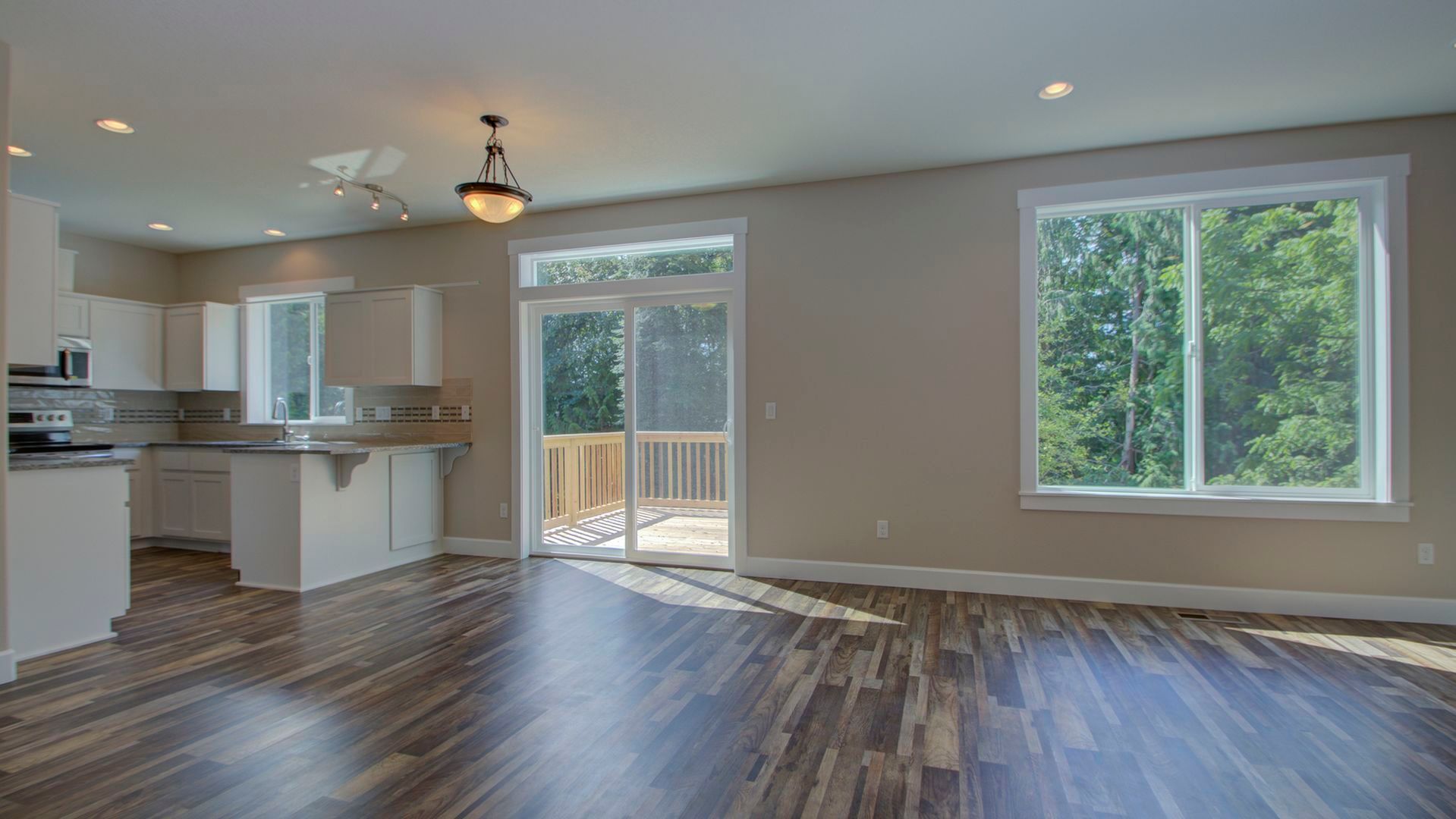 An empty living room with hardwood floors and sliding glass doors leading to a kitchen.