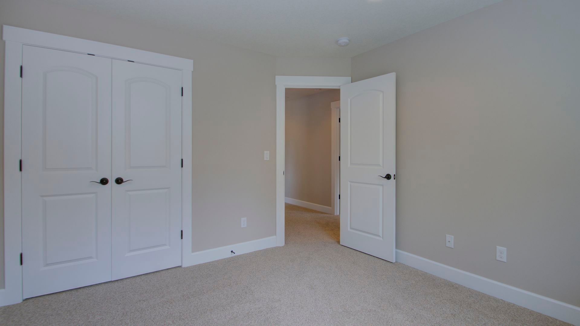 An empty bedroom with a carpeted floor and white doors.