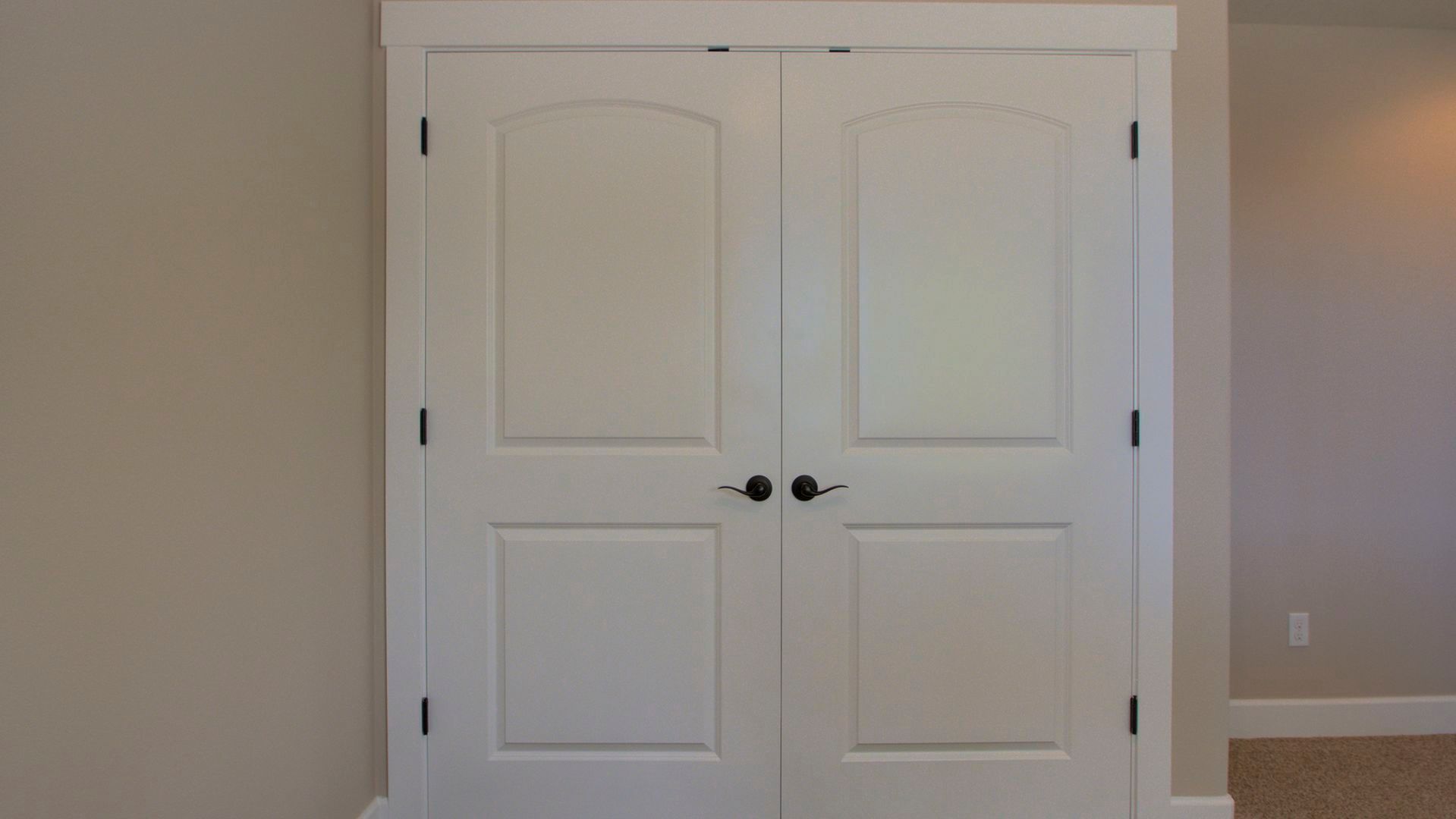 A pair of white doors with black handles in an empty room.