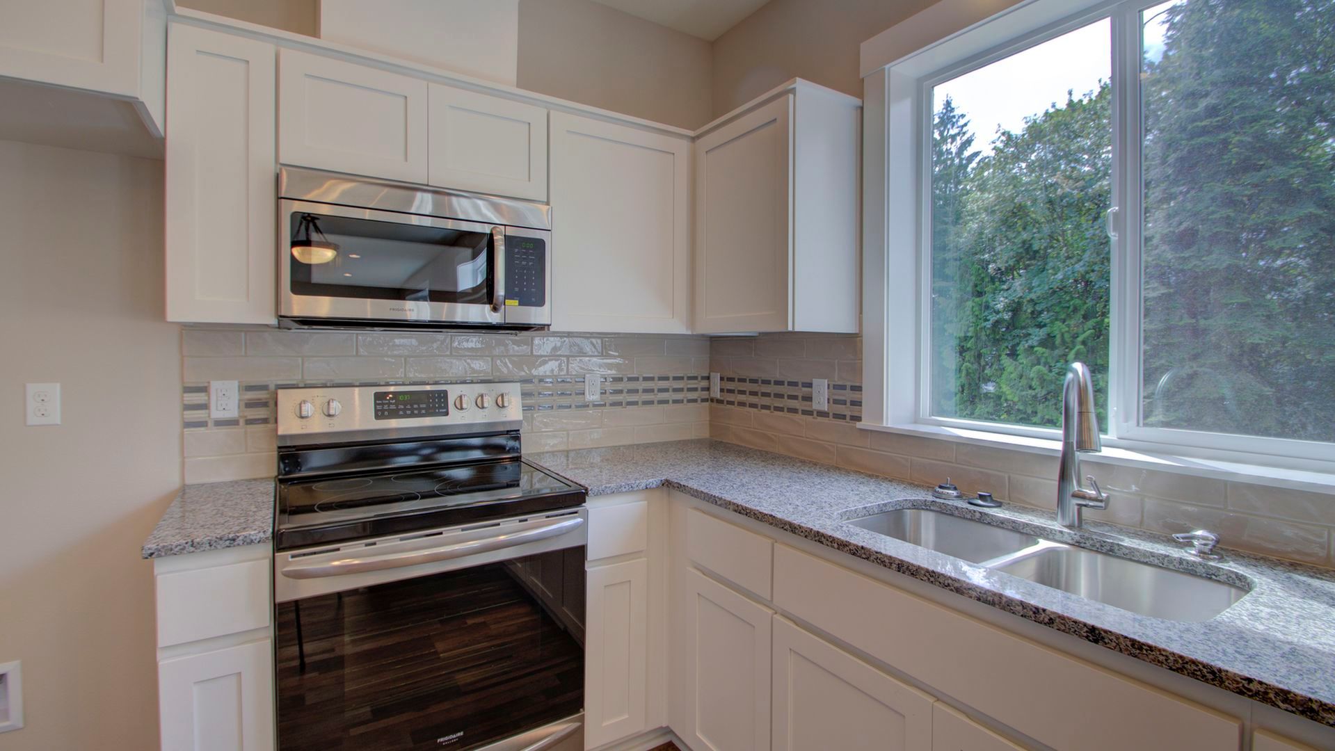 A kitchen with white cabinets , stainless steel appliances , a sink and a window.