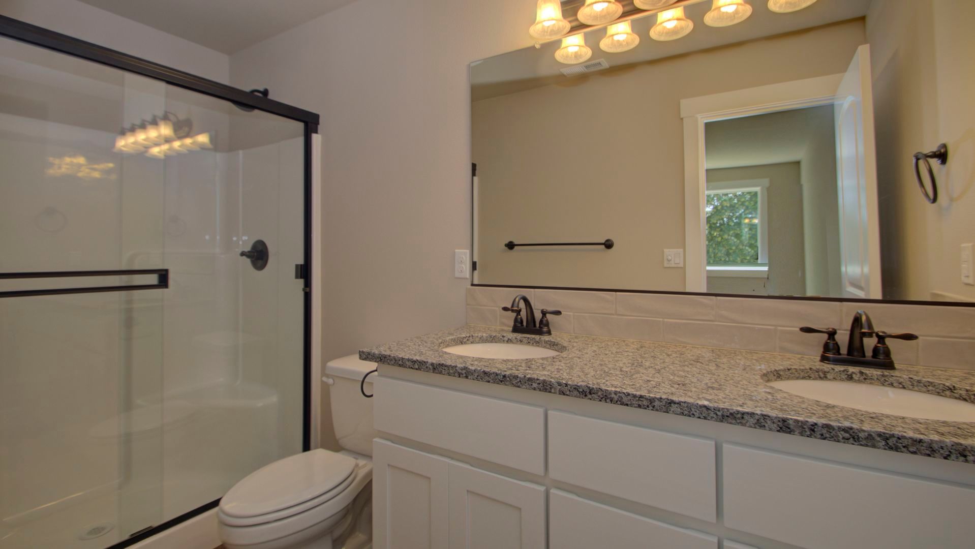 A bathroom with two sinks , a toilet , and a walk in shower.