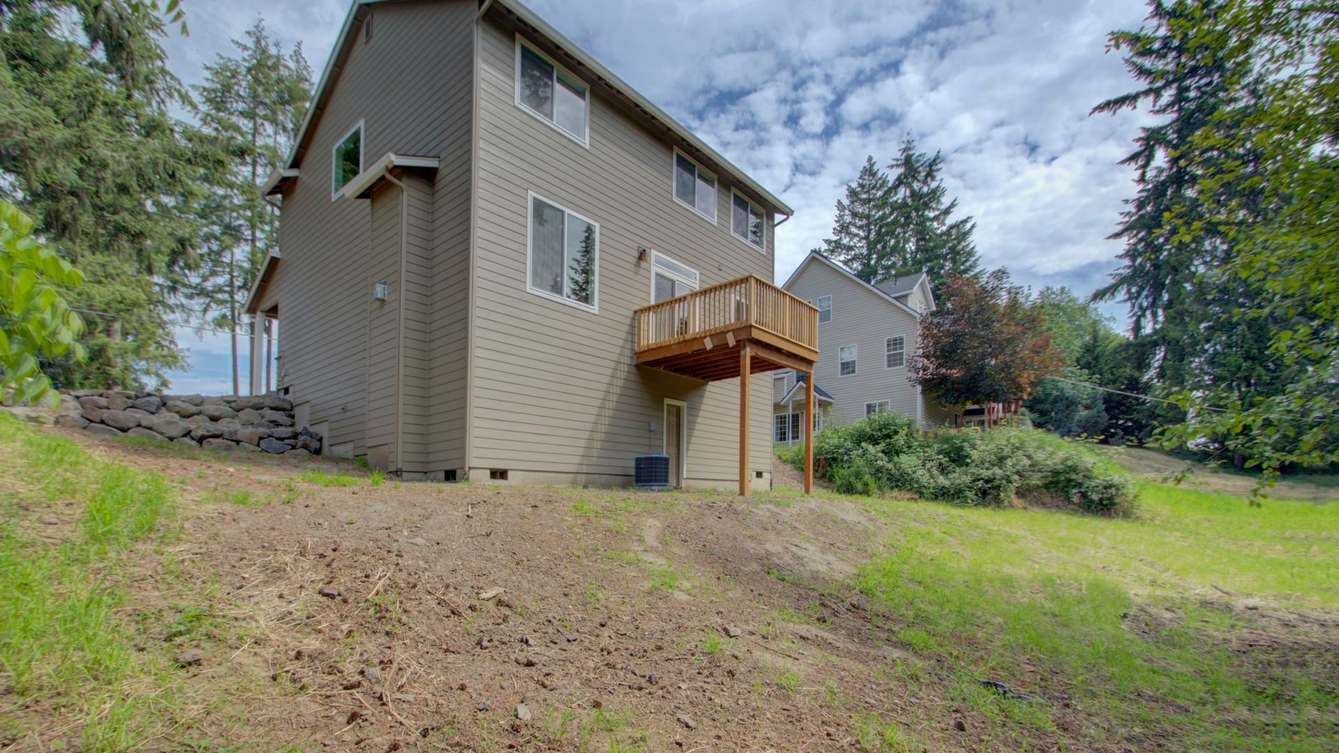 A large house with a deck is sitting on top of a grassy hill.