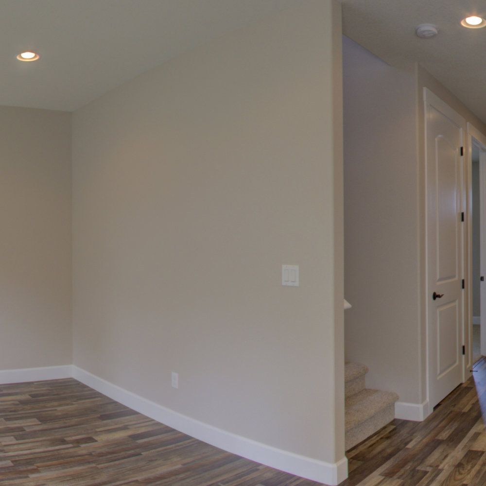 A panoramic view of an empty room with wooden floors and white walls.