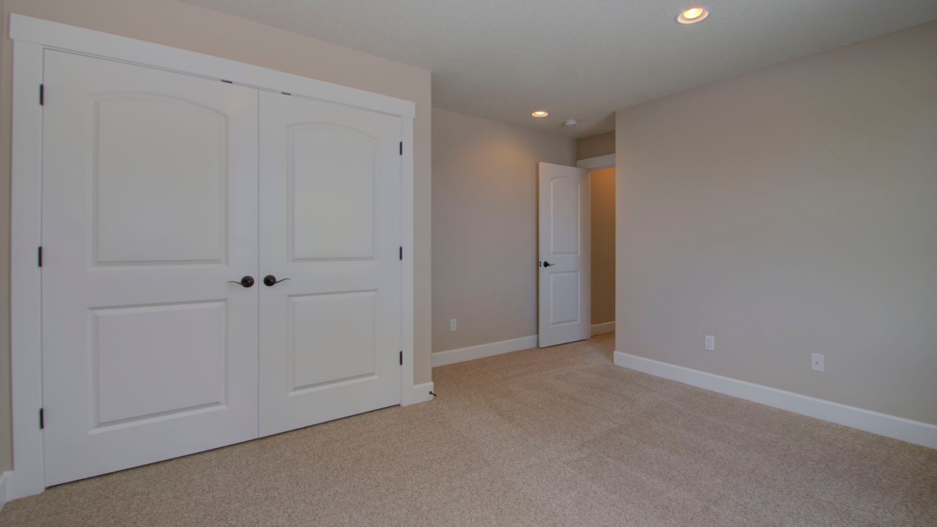 An empty bedroom with a carpeted floor and two closets.