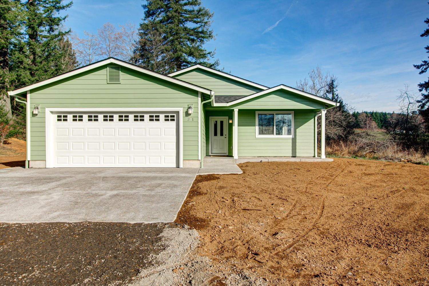 A green house with a white garage door is sitting on top of a dirt field.