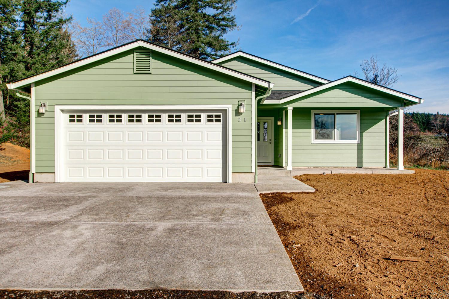 A green house with a white garage door and a concrete driveway.