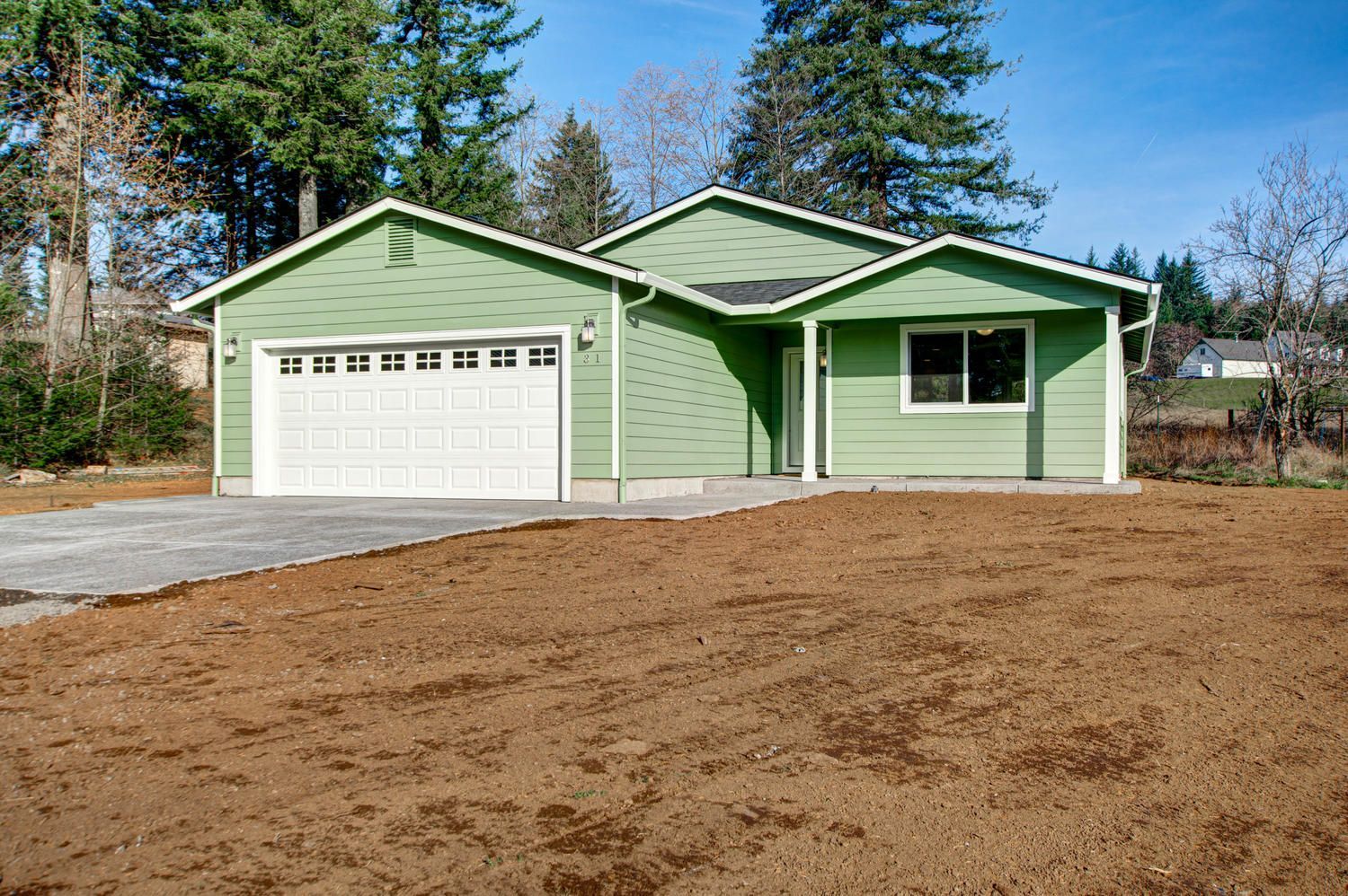 A green house with a white garage door is sitting on top of a dirt field.