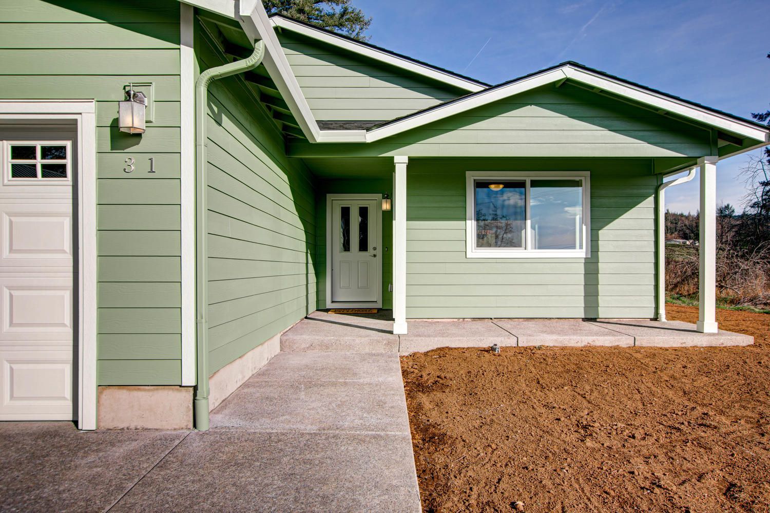 A green house with a white door and a white garage door