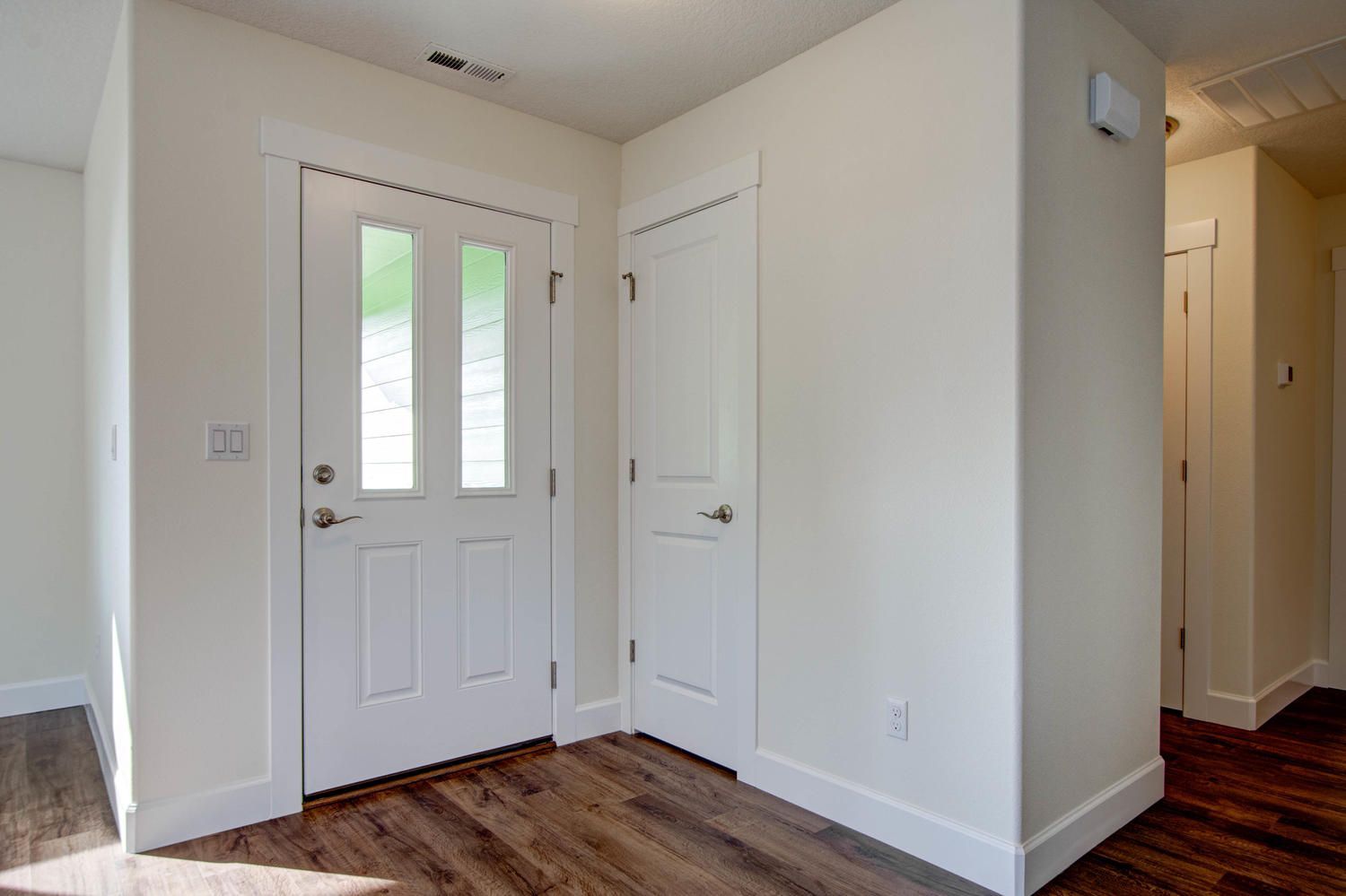 A hallway with a white door and wooden floors in a house.