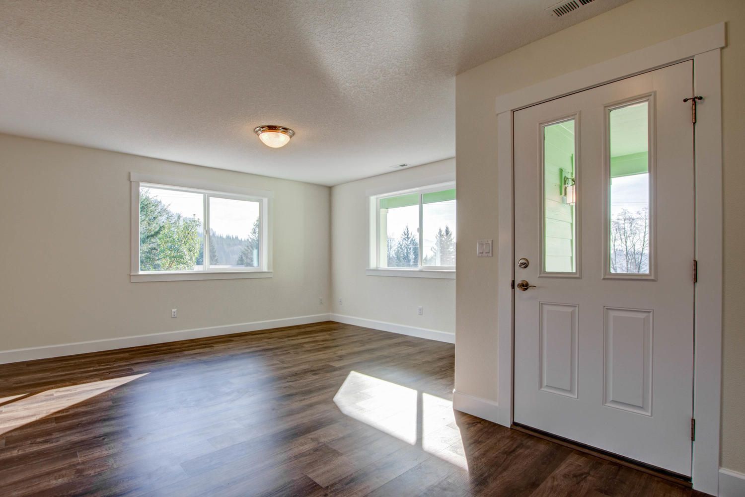 An empty living room with hardwood floors and a white door.