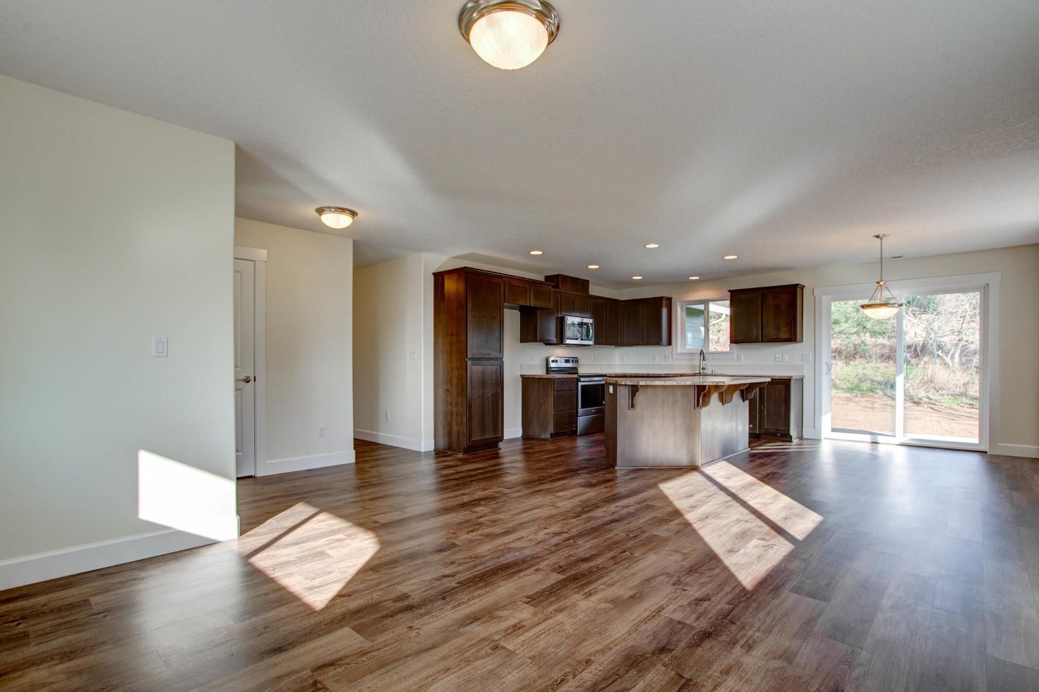 A living room with hardwood floors and a kitchen in the background.