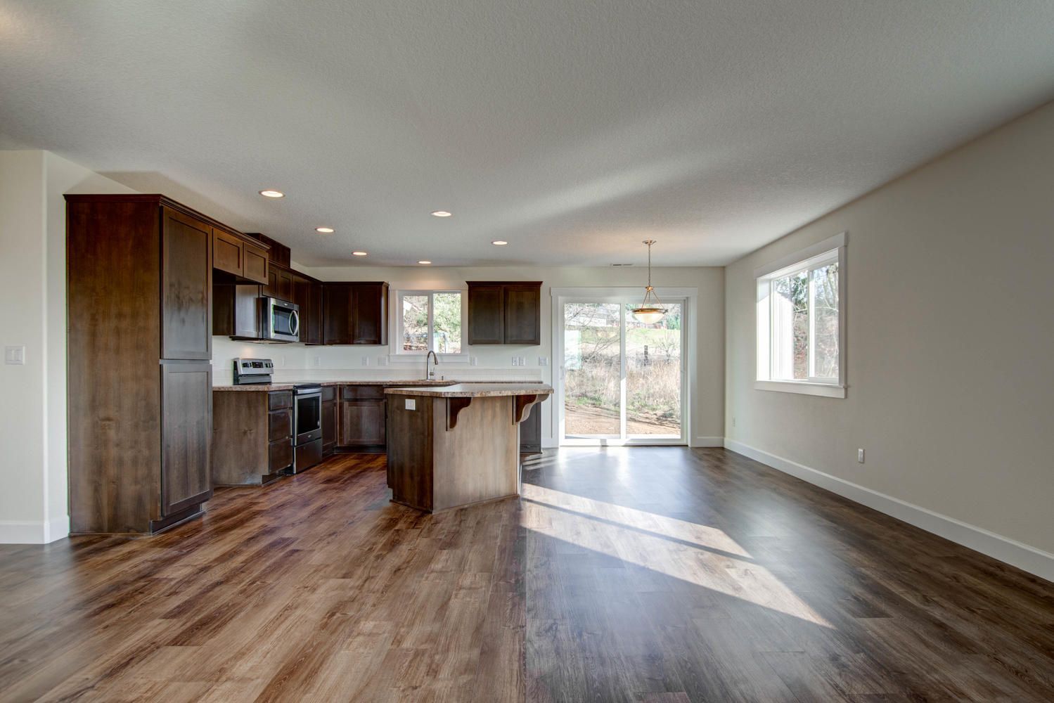 A kitchen and living room in an empty house with hardwood floors.