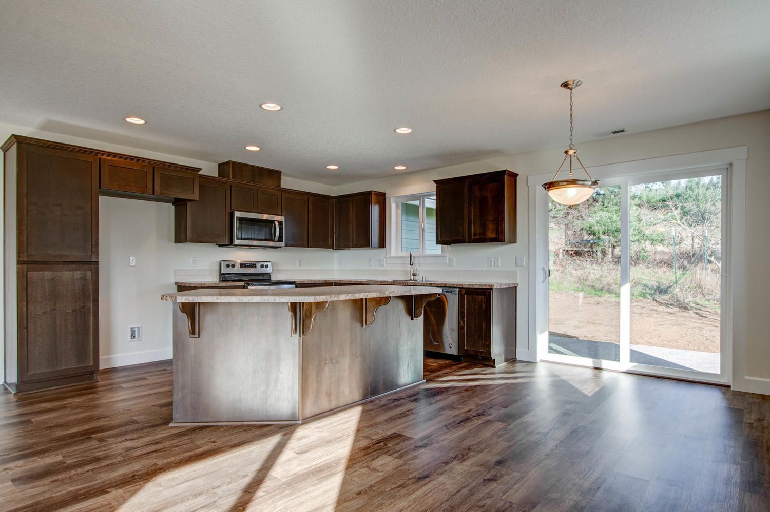 An empty kitchen in a new home with hardwood floors and stainless steel appliances.