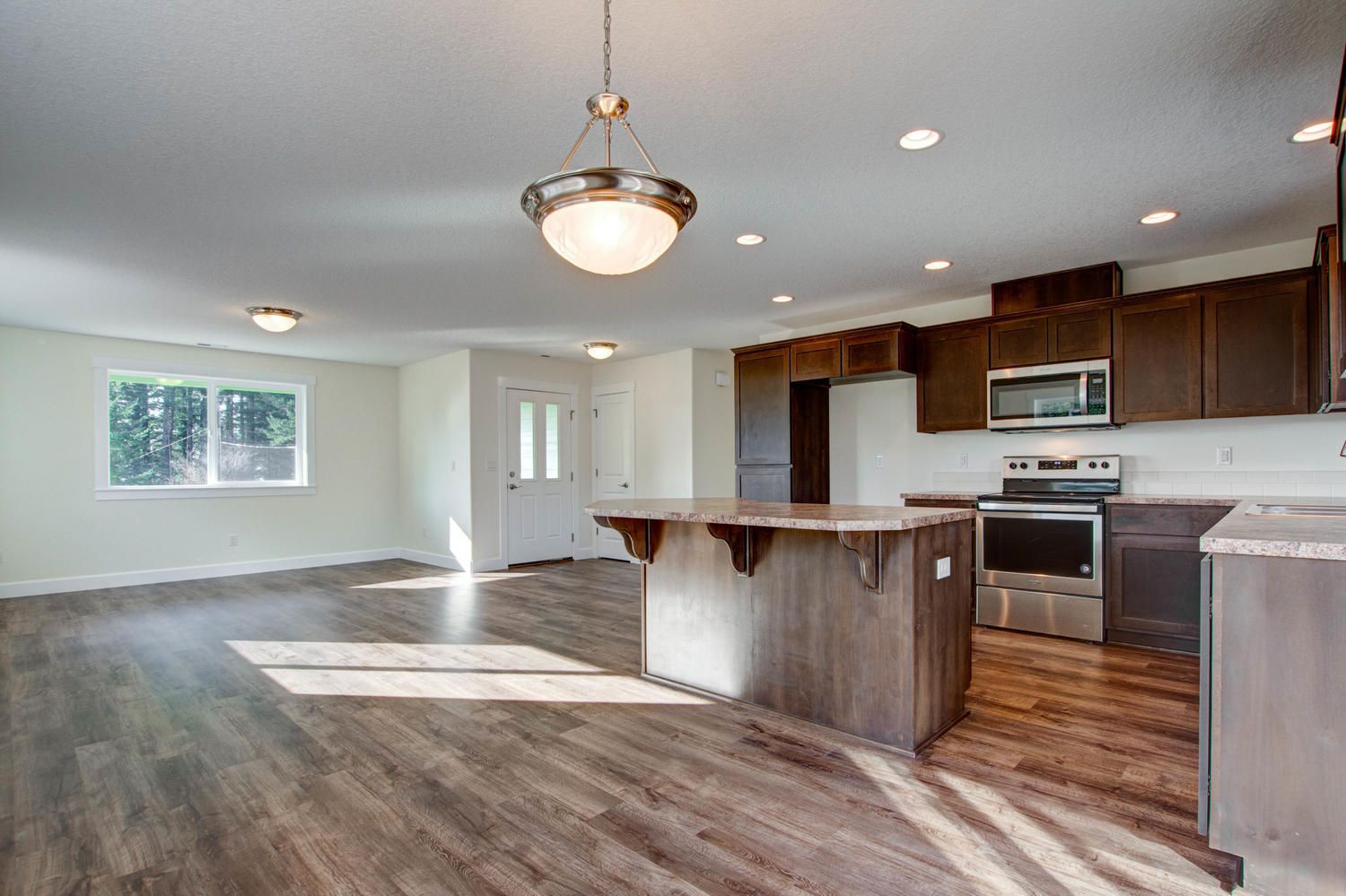 An empty kitchen with hardwood floors and stainless steel appliances.