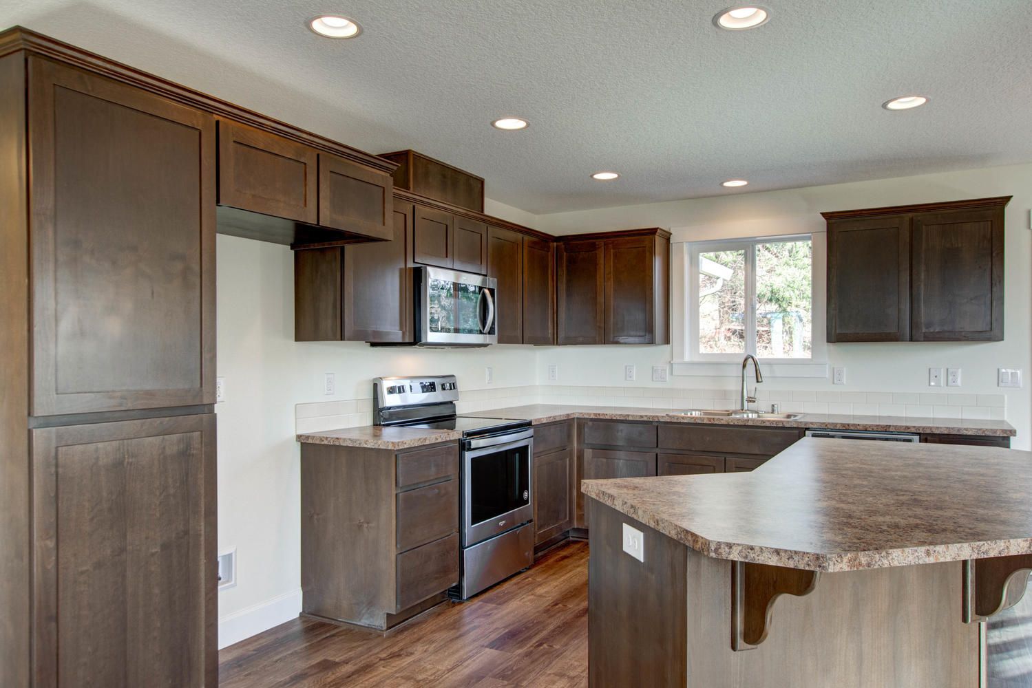 A kitchen with wooden cabinets , granite counter tops , stainless steel appliances and a large island.