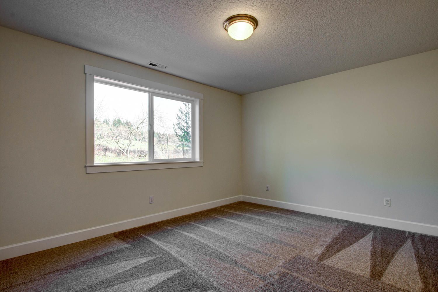 An empty bedroom with a window and a ceiling light.