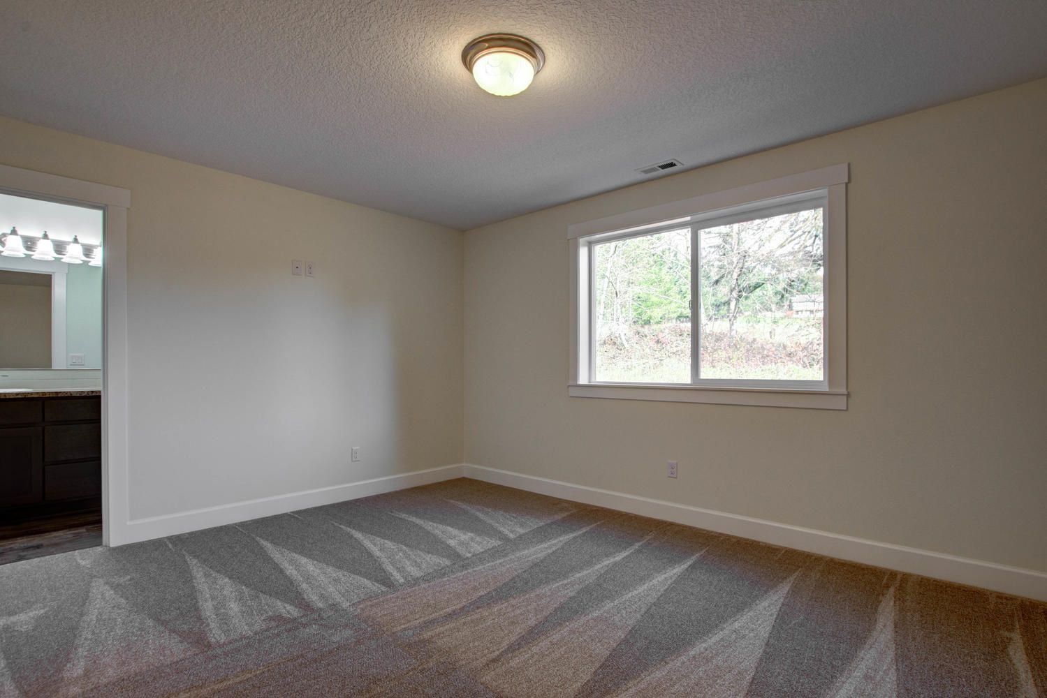 An empty bedroom with a carpeted floor and a window.