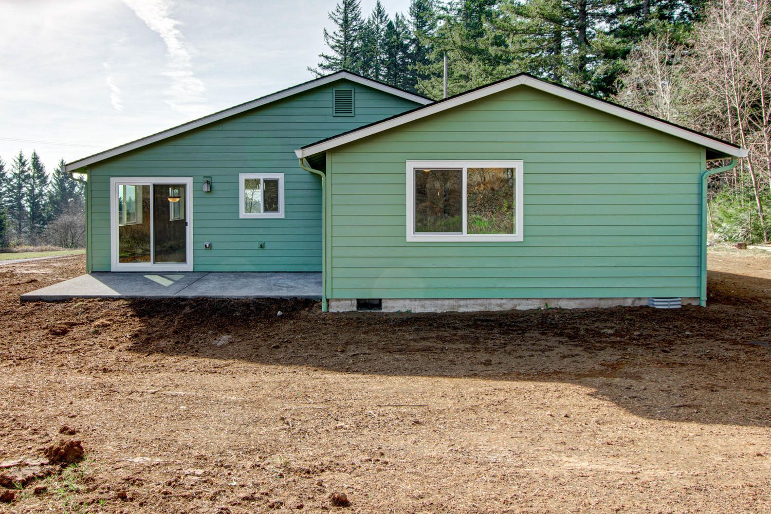 A green house is sitting in the middle of a dirt field.