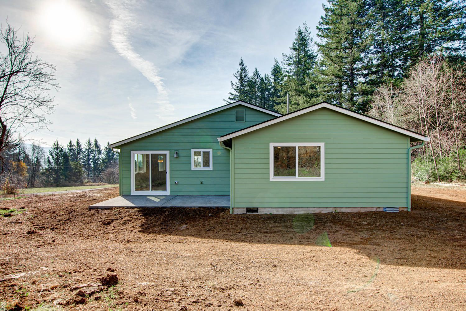 A green house is sitting in the middle of a dirt field.