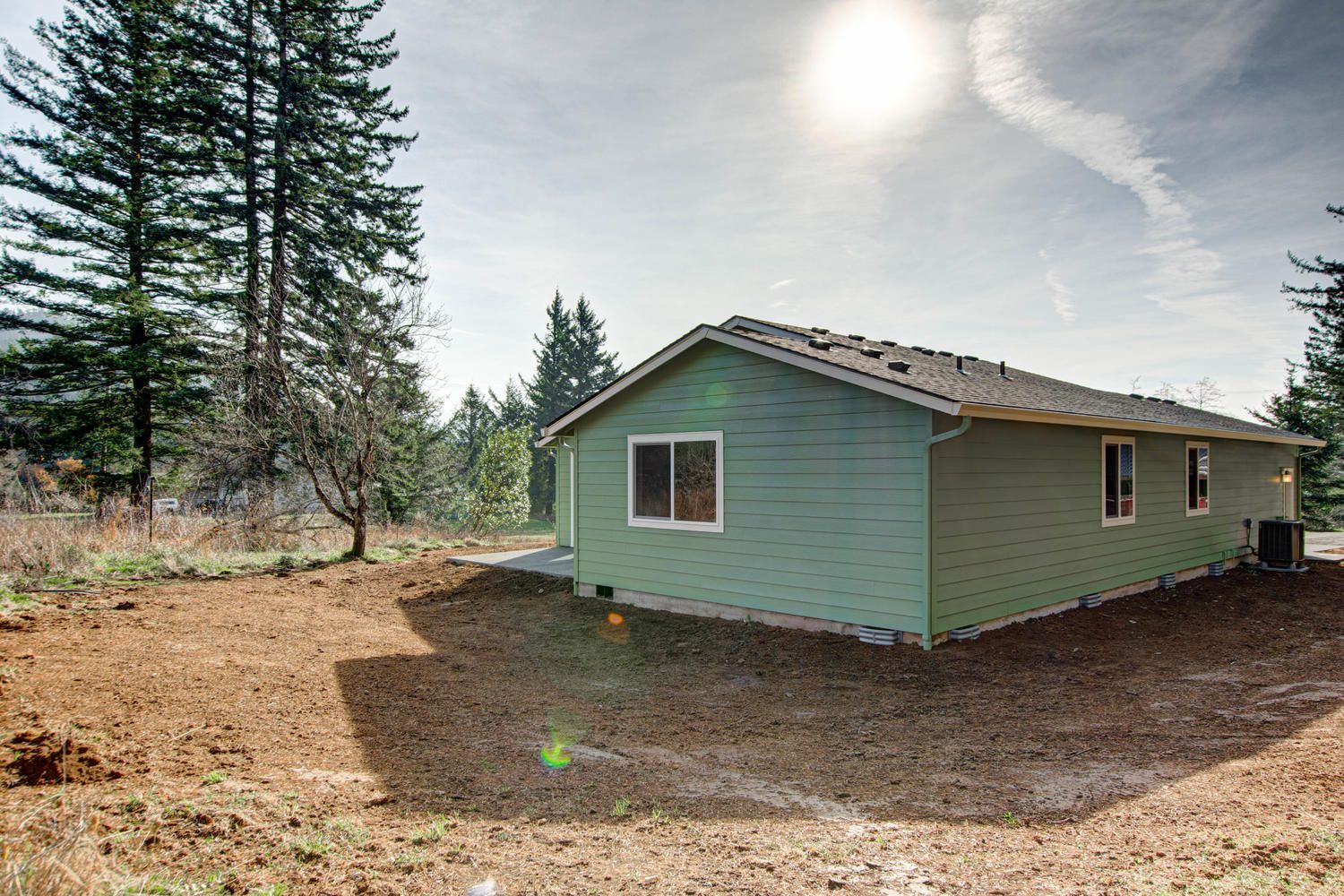 A green house is sitting in the middle of a dirt field surrounded by trees.