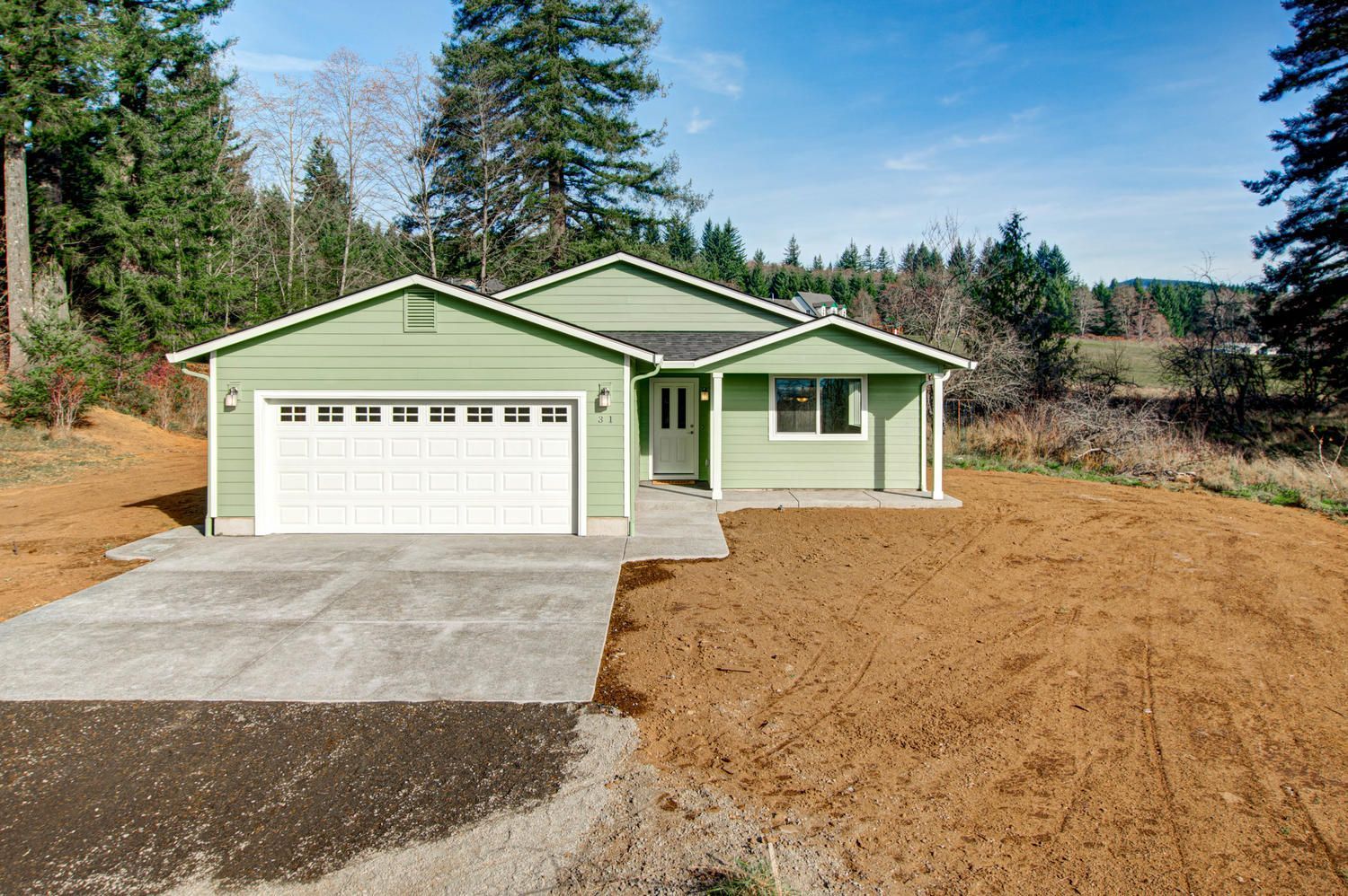 A green house with a white garage door is sitting on top of a dirt hill.