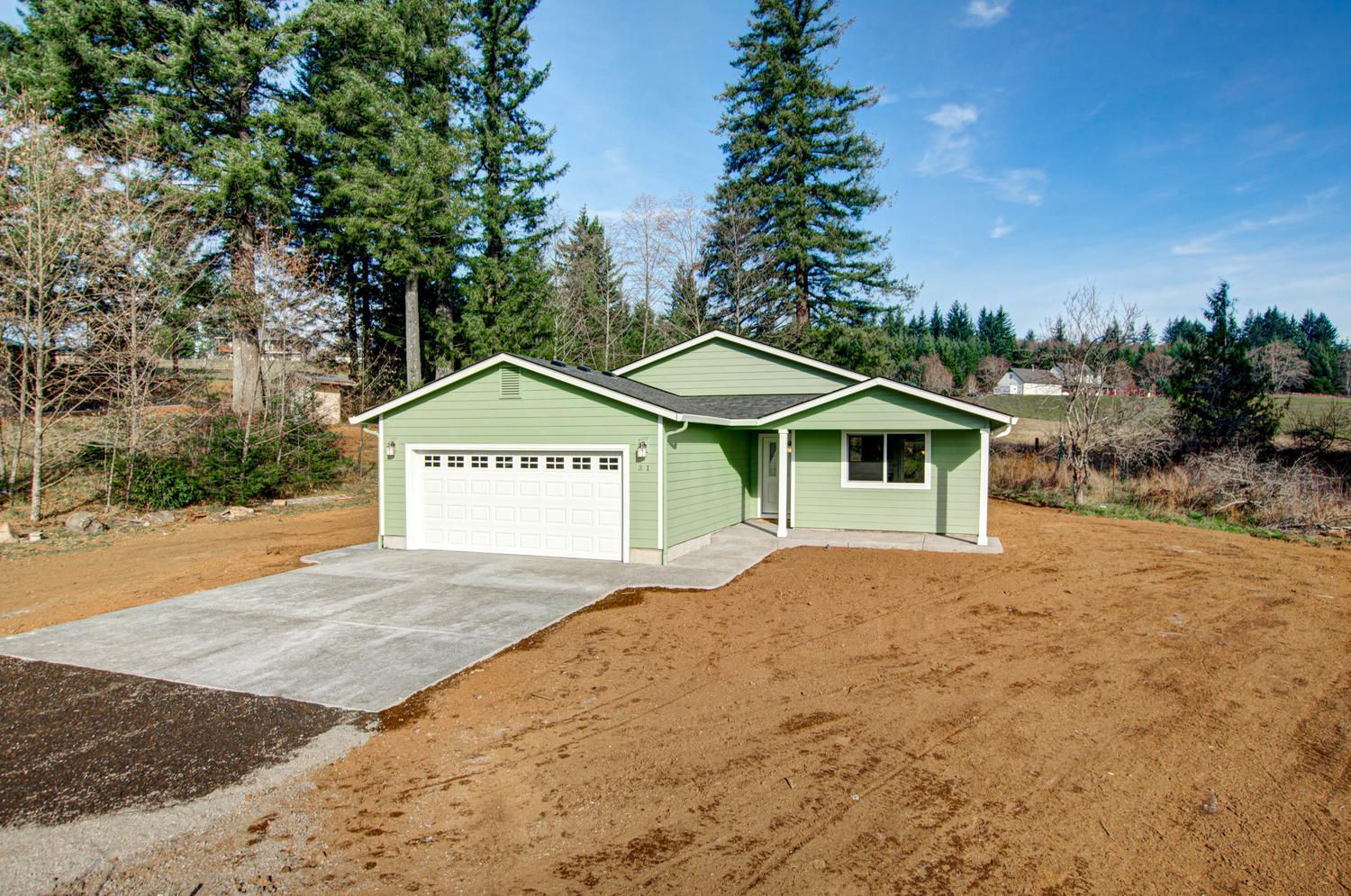 A green house with a white garage door is sitting in the middle of a dirt field.