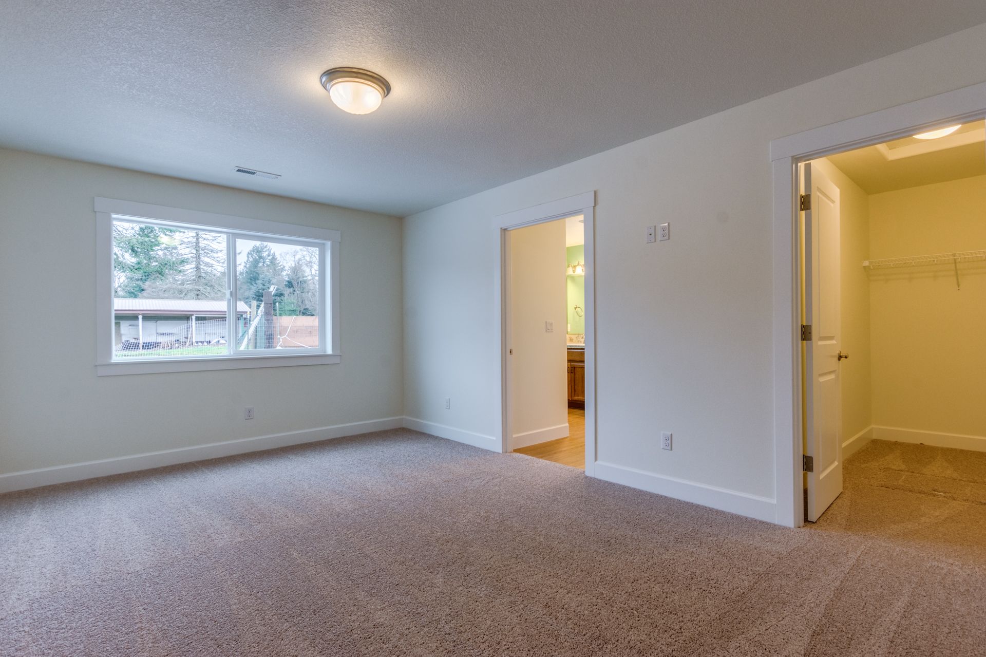 An empty bedroom with a window and a walk in closet.