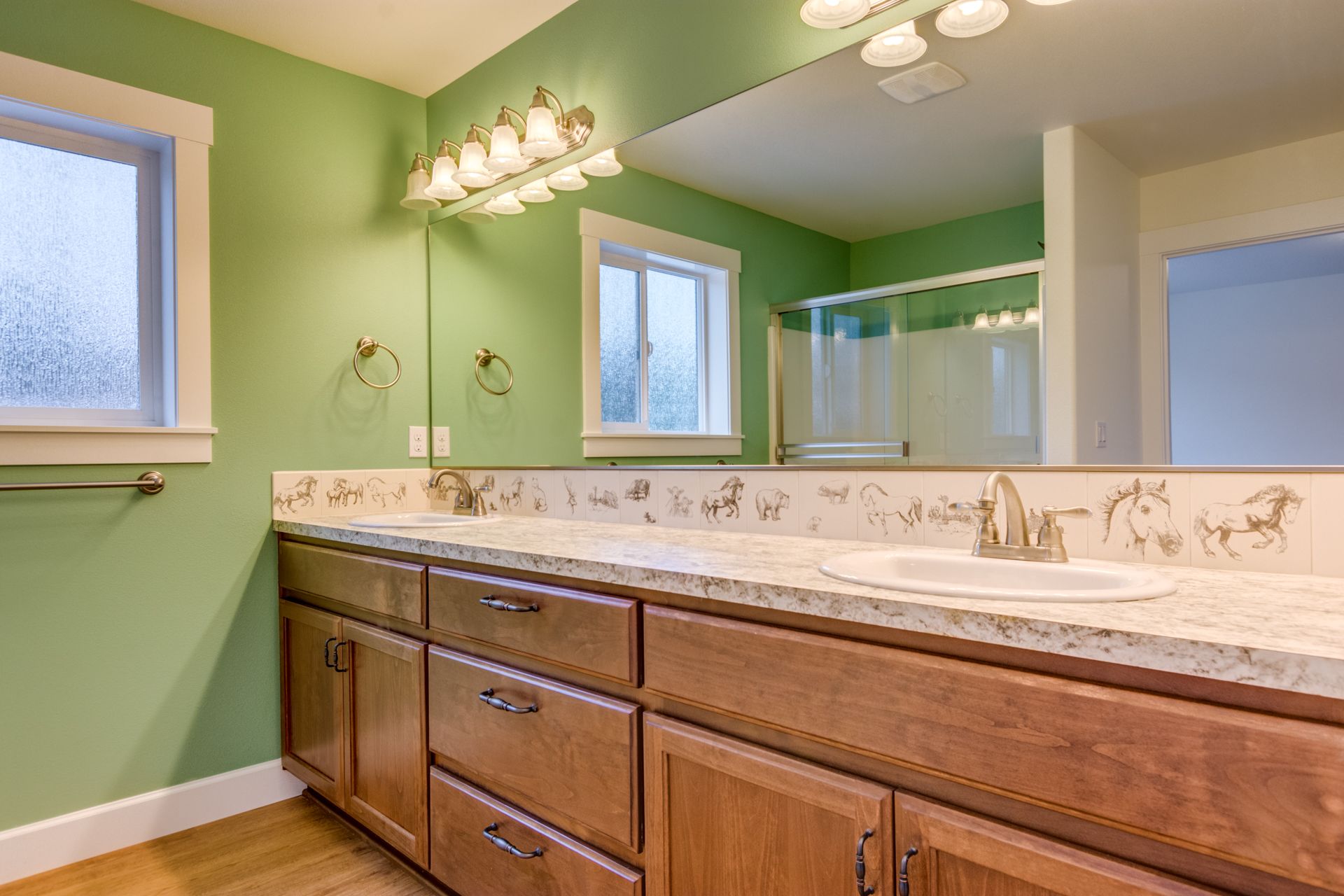 A bathroom with green walls , wooden cabinets , a sink and a large mirror.