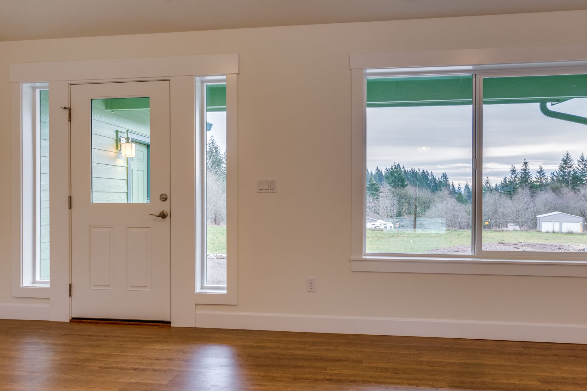 An empty room with a door and two windows with a view of a field.