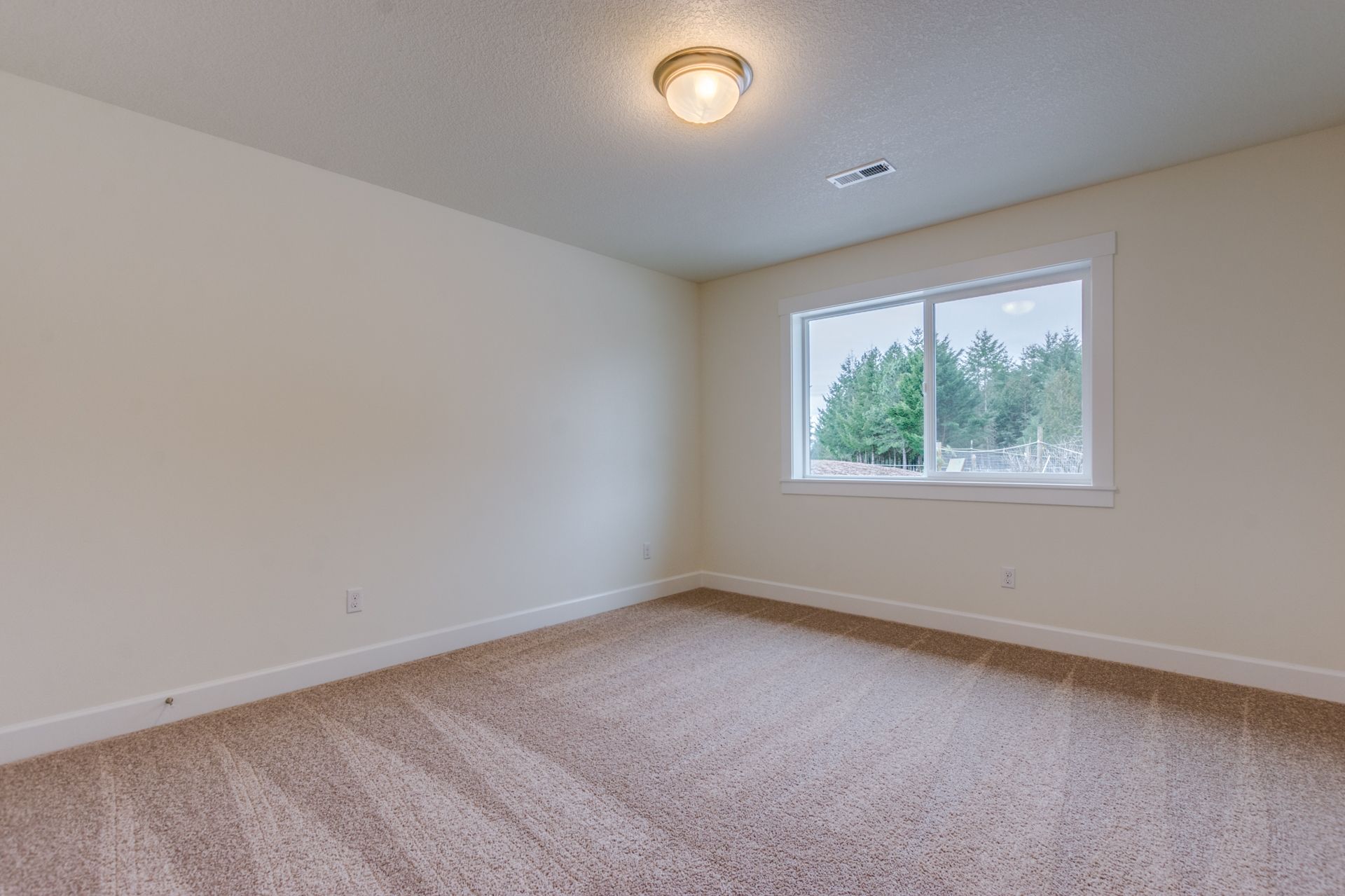 An empty bedroom with a window and a carpeted floor.